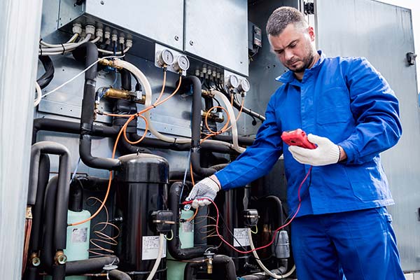 A technician in blue overalls holding a red HVAC diagnostic device